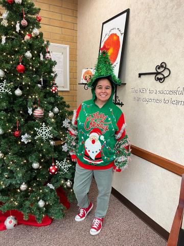 pictured is a teacher wear a Christmas sweater with a Santa and a Christmas tree - with green fringe