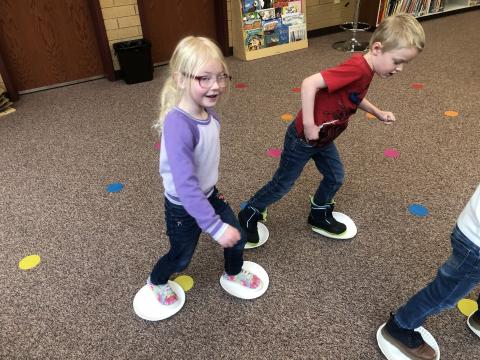 Pictured is students standing on paper plates sliding along the carpet. 